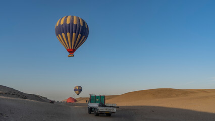 Bright balloons are flying in a clear blue sky. Below, among the sand dunes of the desert, there are cars. Light and shadows. Egypt. Luxor