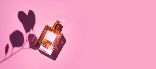 Transparent bottle of perfume on a pink background. Fragrance presentation with daylight.