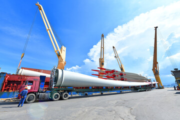 Large wind turbine rotor blades being unloaded from a ship onto a telescopic trailer for onward...