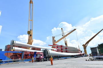 Large wind turbine rotor blades being unloaded from a ship onto a telescopic trailer for onward...