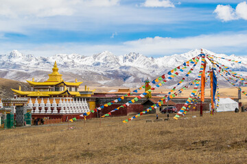 Tibetan buddhist monastery in Tagong, Colorful Tibetan Buddhist prayer flags hung on a pole and the snowy mountain"Yala"  at the background. China , Sichuan.