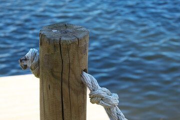 Railing on the shore of the lake. Rope in a wooden pole.
