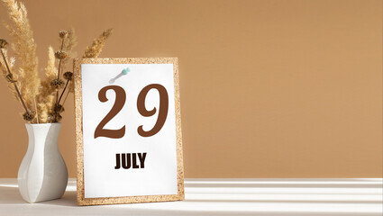 july 29. 29th day of month, calendar date.White vase with dead wood next to cork board with numbers. White-beige background with striped shadow. Concept of day of year, time planner, summer month