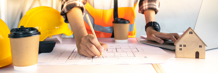 Architect is editing a construction drawing with a pencil.Professional home design Using a laptop in house and building construction projects.Banner cover website design.Expert engineer,worker,coffee.