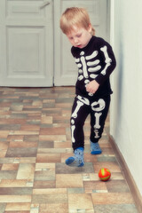 A child in a skeleton costume plays football in the hallway of the house - 501265872