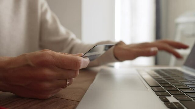 Irritated young caucasian girl sitting with computer and credit card on couch in kitchen room, can not make purchase, not enough money. Unhappy client dissatisfied with online payment banking service.