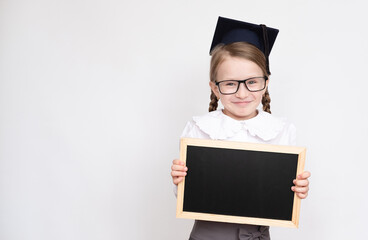 Little girl in student hat and glasses holding empty blackboard on white background back to school