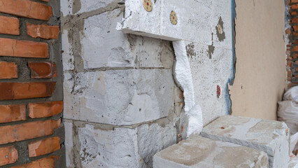 Ruined corner of the house close-up. Aerated concrete and red brick wall. Wall covered with...