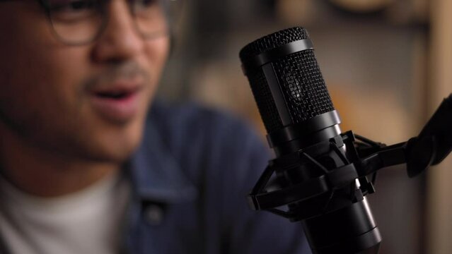 Close-up condenser microphone of content creator man host streaming his a podcast on laptop with headphones interview conversation at night broadcast studio. Male blogger recording voice over radio
