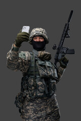 Shot of joyful serviceman from ukraine posing with mobile phone against grey background. Information war.