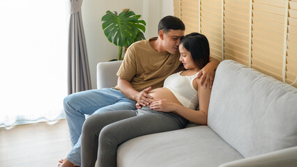 Young pregnant woman with husband embracing and expecting a baby at home