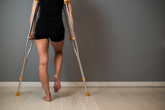 Woman with injured leg using crutches on grey background, closeup. Space for text