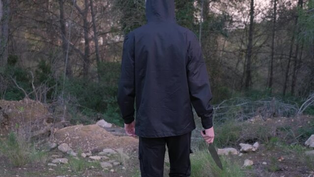 A man with a knife in the forest. The maniac pursues the victim and prepares to attack