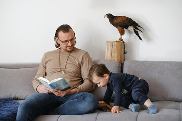 Father with child and wild bird buzzard sitting on the coach, reading, playing on smartphone....