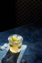 ice tea with ice cubes, lime, mint leaves in the glass on gray stone background