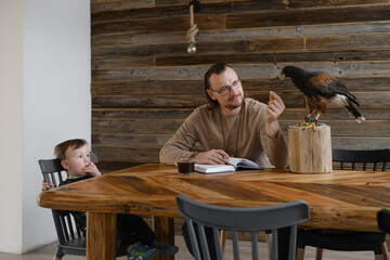Man is working, writing with wild bird at home by the table, child sitting. Making noted, memories,...