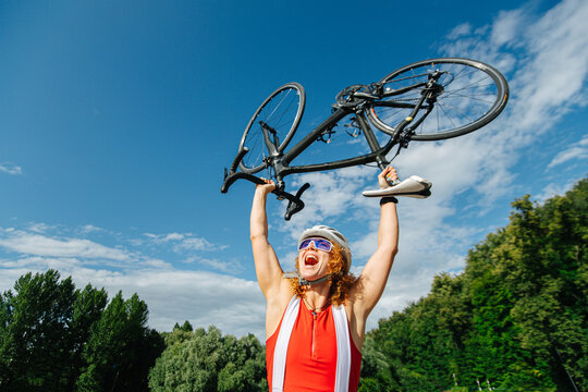 Triumphant low angle picture of a woman cyclist lifting her bike over head