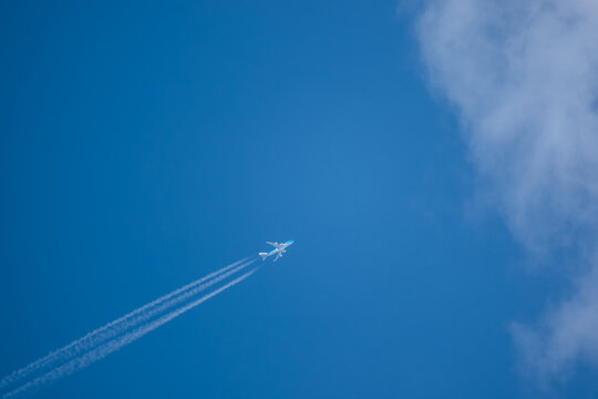 diagonal lower left to upper right high altitude contrails from a four engine KLM Boeing 747-400 Cargo Jumbo jet aircraft entering cloud blue sky