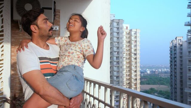 A pretty little girl with a ponytail in her father's lap - love and affection  comfortable. A loving Indian father chatting with his daughter while standing outdoors - father-daughter bonding  balc...