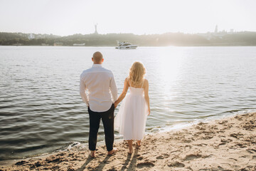 Wedding photosession at sunset of a beautiful couple, the bride in a white dress, and the groom in a white shirt and black trousers