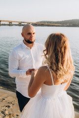 Wedding photosession at sunset of a beautiful couple, the bride in a white dress, and the groom in a white shirt and black trousers