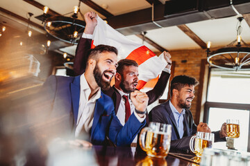 Group of friends at the pub watcing football game and drinking beer
