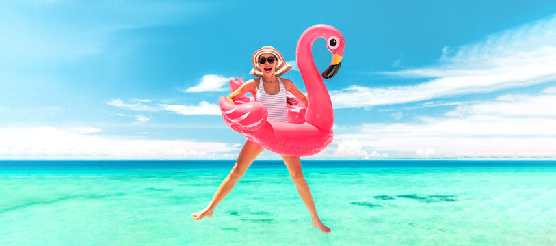 Vacation beach woman jumping of joy with pink flamingo pool float for summer holidays on ocean banner background. Fun travel excited girl for luxury Caribbean holiday panoramic