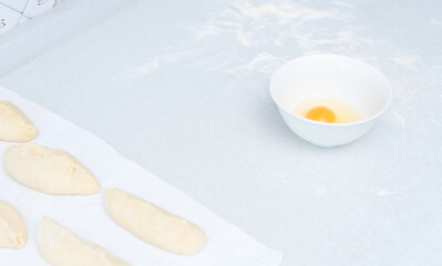 White bowl with raw egg, raw pies with apple filling and flour on a white kitchen table. Selective focus. Cooking at home concept. Tradition home-made food