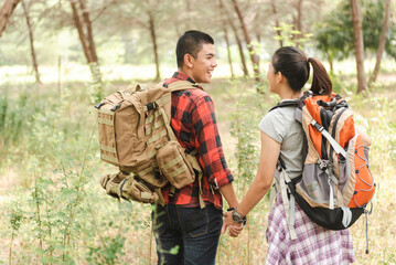Hand in hand, an Asian backpacker couple enters the forest.