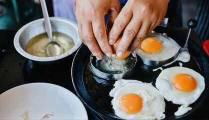 Hands cracking eggs into a heated pan mold. to prepare fried eggs.