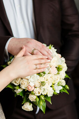A newly weding couple place their hands on a wedding bouquet showing off their wedding rings.