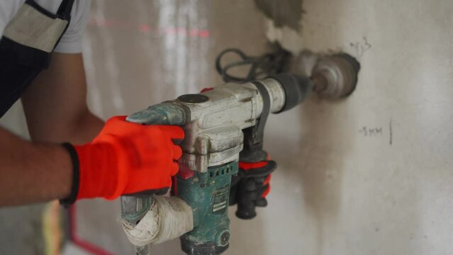 Electrician man boring hole in wall for socket using laser level, working power drill, jackhammer with cylindrical nozzle. Preparation for instsling electrical wires, construction work in apartment.