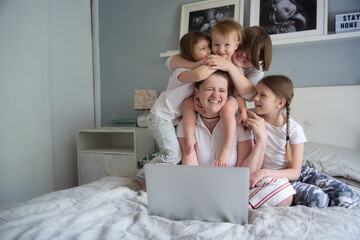 Mom and 4 children are looking at a laptop, watching a movie together. Mom freelancer working at home with children, motherhood and work, watching cartoons together