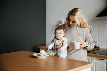 Mother and son at the kitchen, wearing pajamas. Woman holding baby and drinking coffee in the morning.