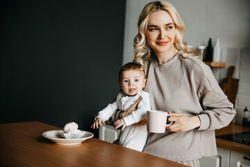 Mother and son at the kitchen, wearing pajamas. Woman holding baby and drinking coffee in the...