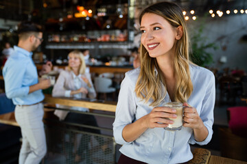 Portrait of happy young business woman drinking coffee in a break. In the background, her colleagues