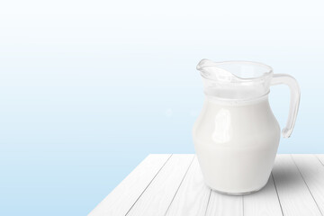 Glass jug of fresh milk on white wooden table with blue background. Copy space.