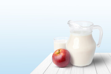 Glass of milk and apple fruit on wooden table with blue background.