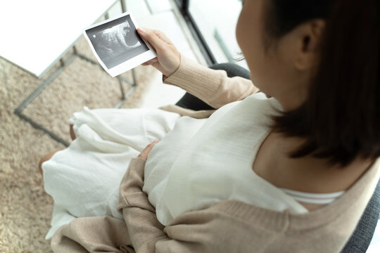 Asian pregnant woman looking at ultrasound picture at home