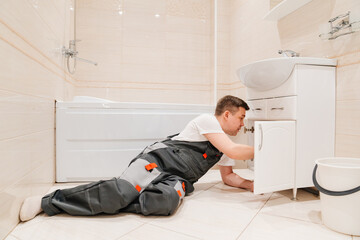 A male plumber repairs siphon under the sink in the bathroom.