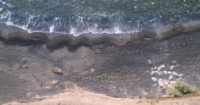 Drone shot looking down at waves coming on the black sand beach in Cap d'Agde FR