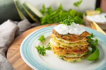 Zucchini pancakes with herbs and sour cream on a blue plate close-up. Vegetarian dish