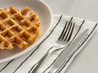 Cabbage waffles with cheese, cotton striped napkin, fork and knife