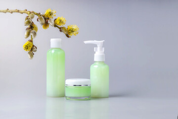 containers for cosmetics and a branch with white willow earrings on a gray background