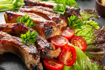  Baked pork ribs with vegetables, mustard and ketchup on gray background close up