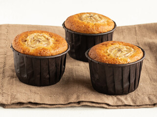 Banana cupcakes in the brown paper baking forms on beige linen cloth, high key, close up
