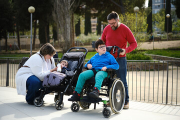 Mother and father enjoying a family day in the park with their baby and a disabled son in...