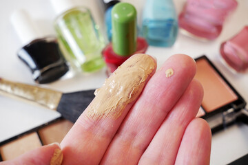 beige concealer in hand on set of cosmetic makeup products background Nail polish, mascara, lipstick, eye shadows, brush, powder, lip gloss