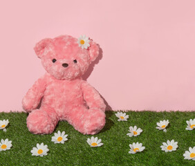 Spring creative layout with pink teddy bear sitting on grass with white flower heads and pastel pink background. 80s or 90s aesthetic fashion toy concept. Minimal romantic summer idea.