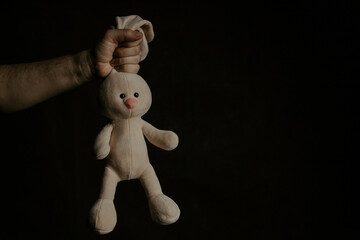 Hand holds a plush rabbit. Abuse, violence or punishment concept
